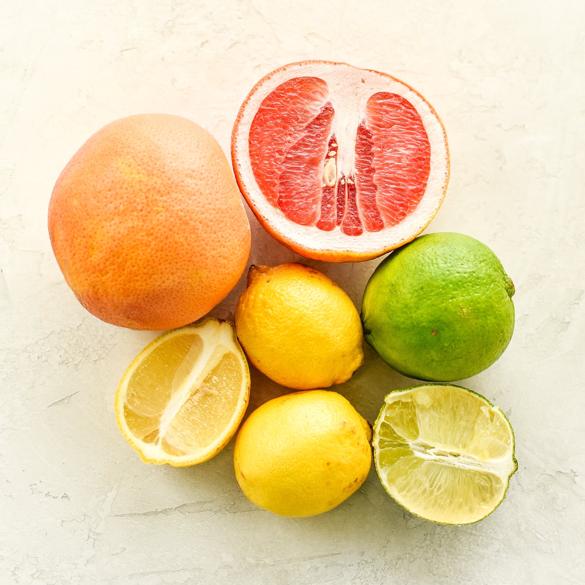 Citrus fruits laid out on a counter viewed from above - including grapefruit, lemons and limes. Some are cut in half.