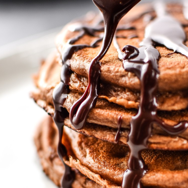 Close up of drizzling chocolate ganache on a stack of double chocolate peppermint protein pancakes.
