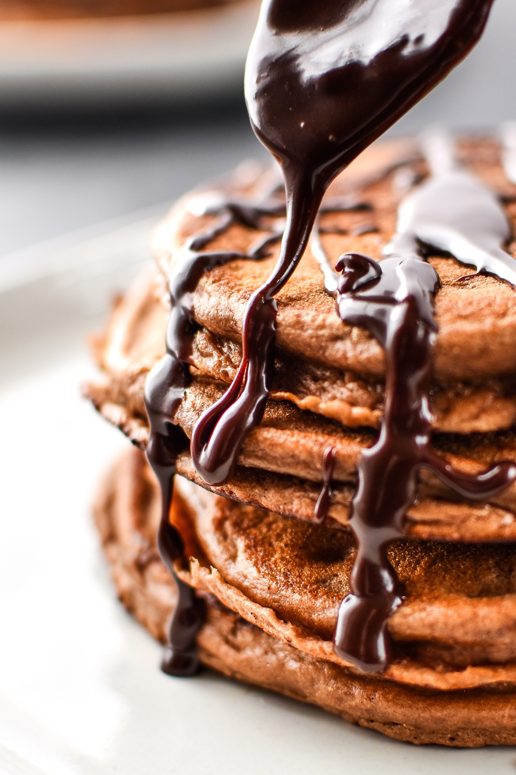 Close up of drizzling chocolate ganache on a stack of double chocolate peppermint protein pancakes.