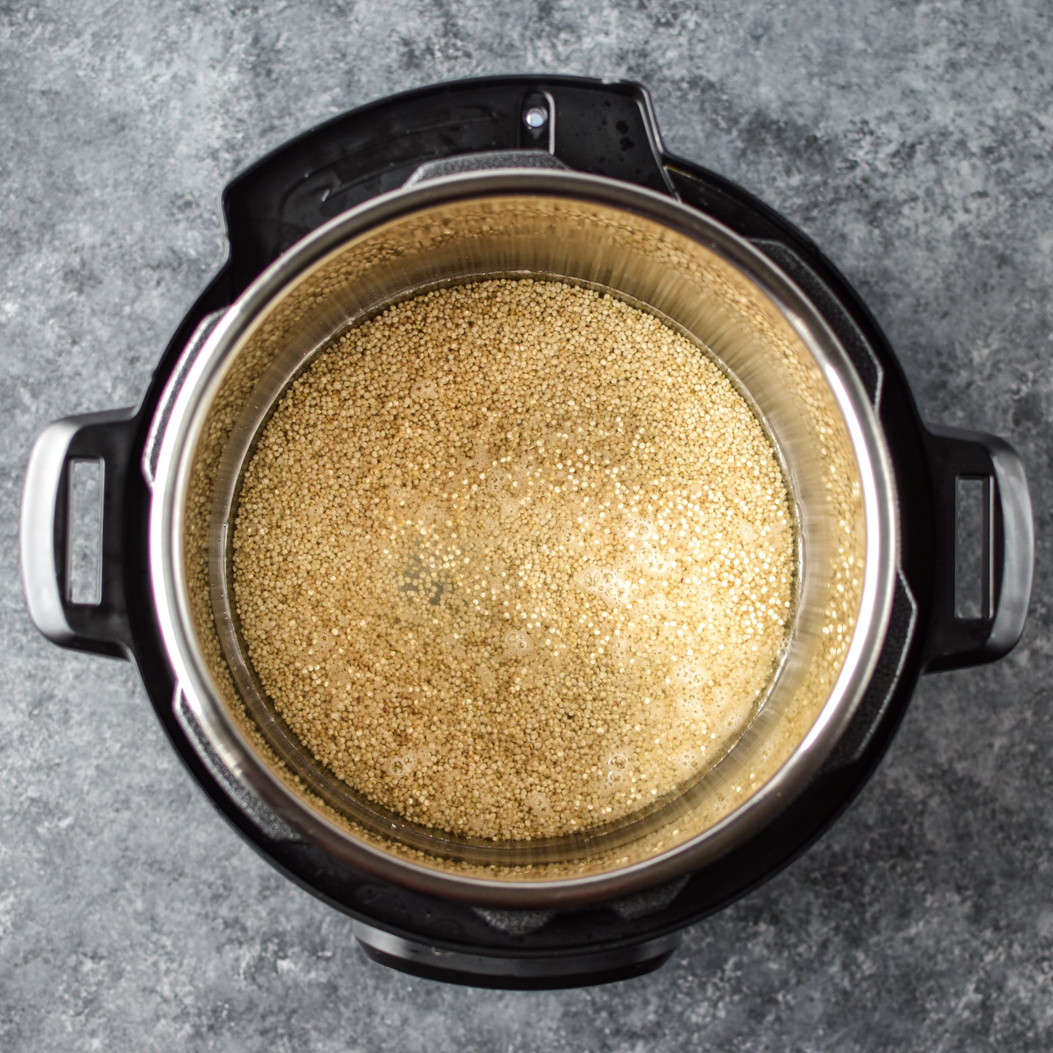 Instant pot with quinoa seen from above, uncooked and ready to be plugged in. 