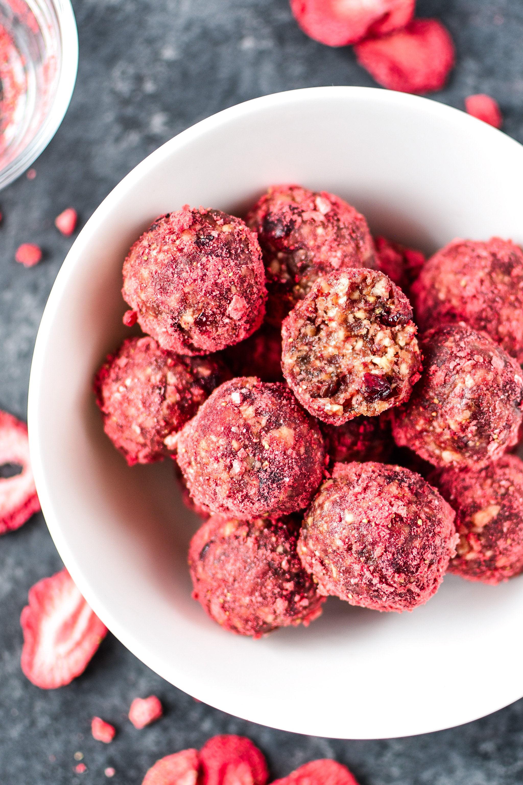 A white bowl of Spiced Berry Bliss Balls with a bite taken out of one.