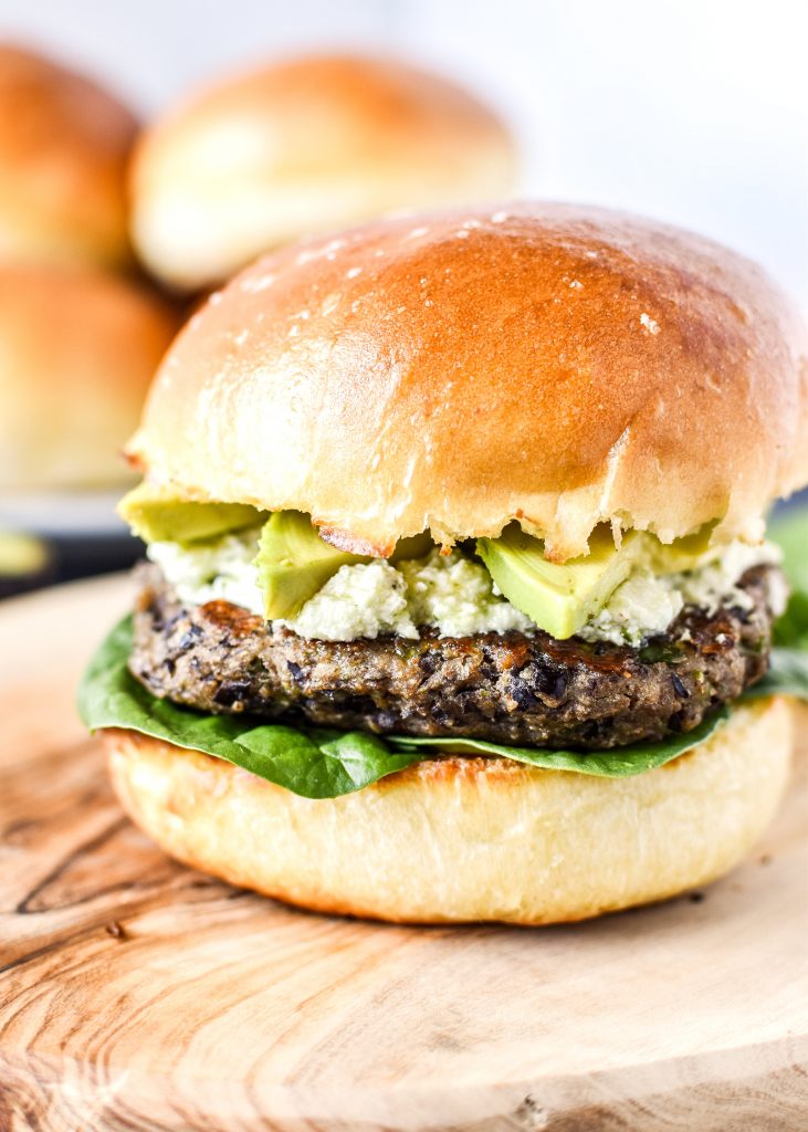 spicy black bean burgers with avocado and pesto goat cheese on a bun.