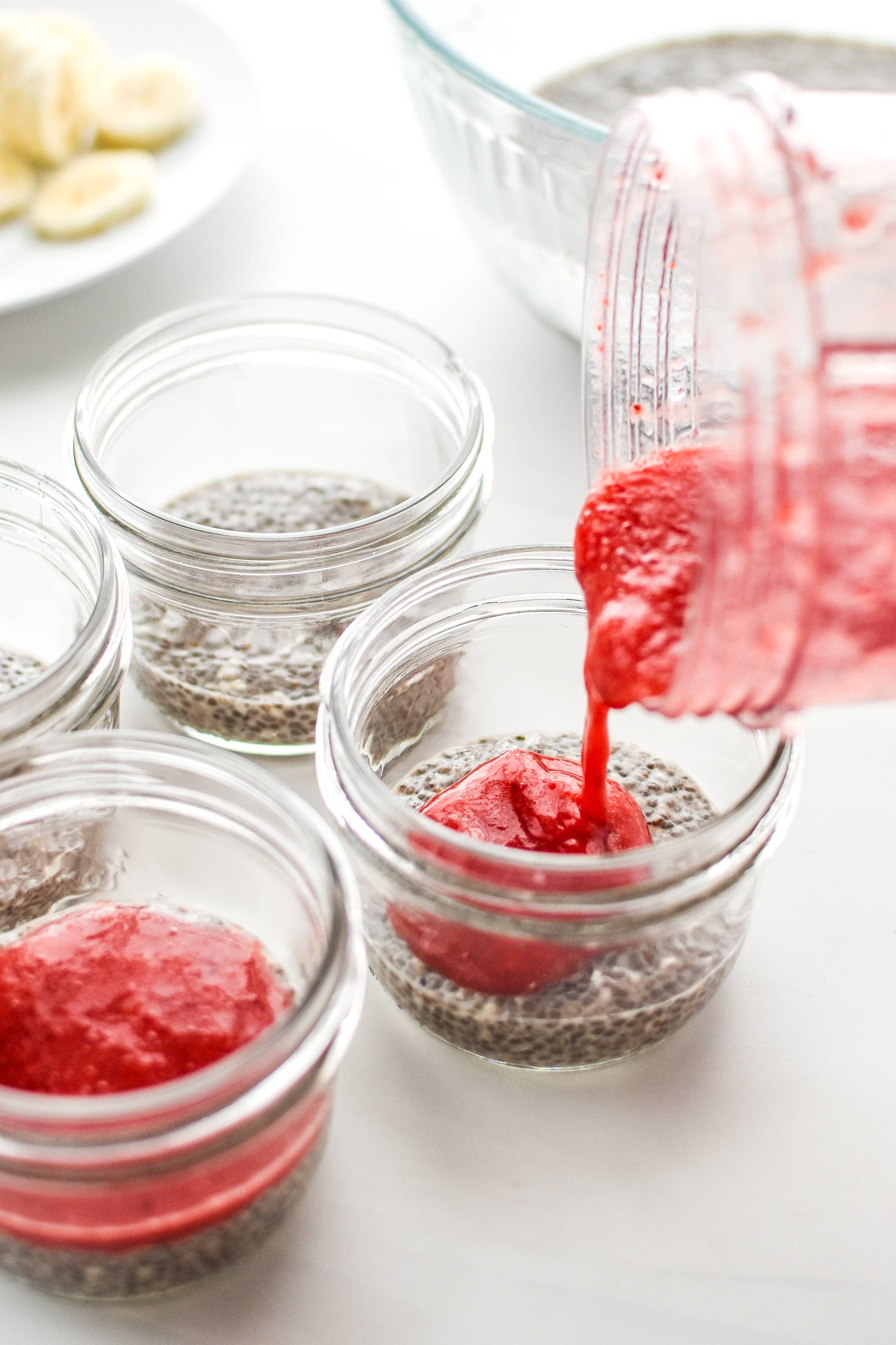 Pouring strawberry puree to the chia pudding breakfast parfaits to make the fruit later