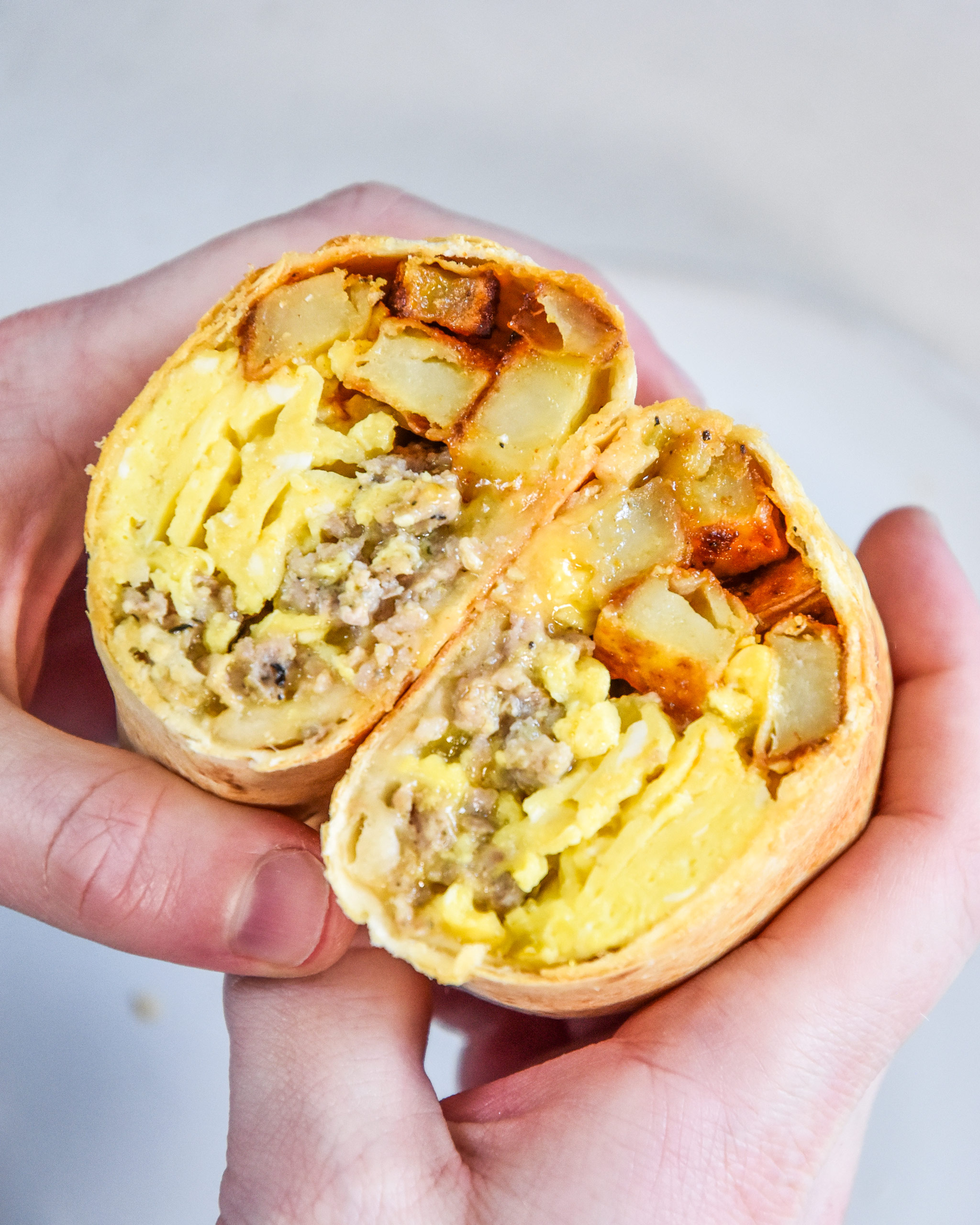 an air fryer breakfast burrito cut in half in someone's hands