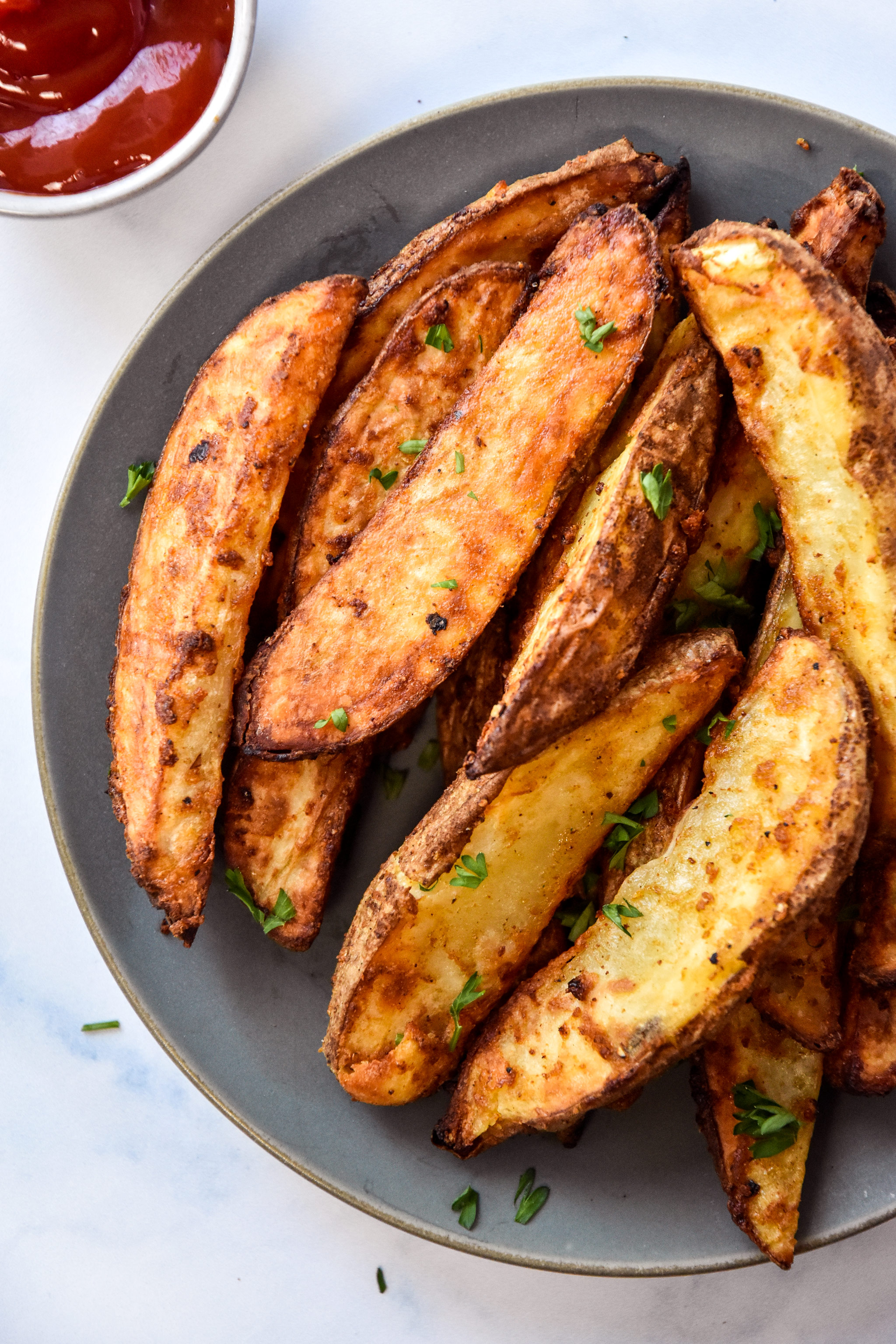 air fryer jojo potato wedges on a plate with parsley sprinkled on top.