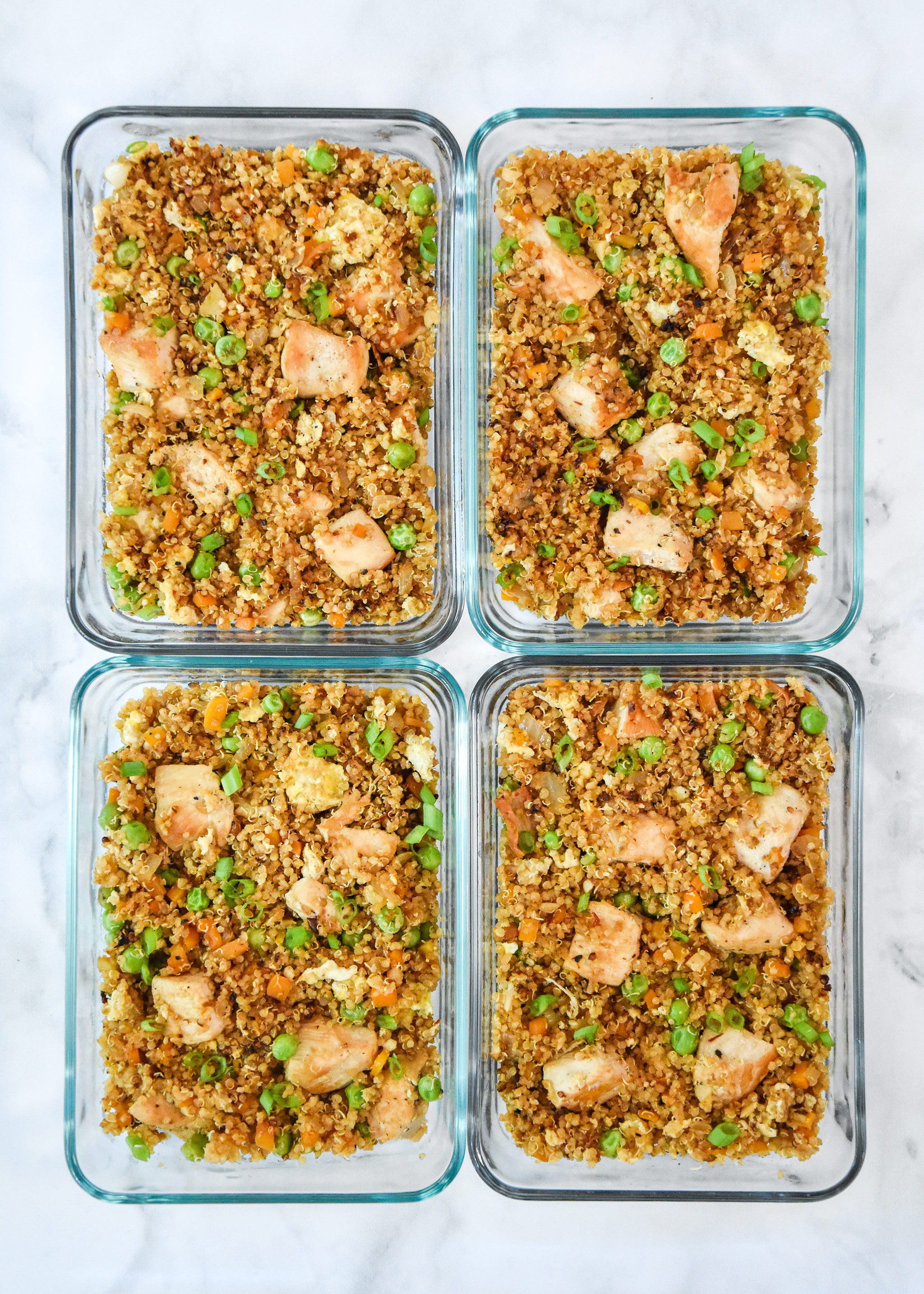 four glass meal prep containers of chicken quinoa fried rice.