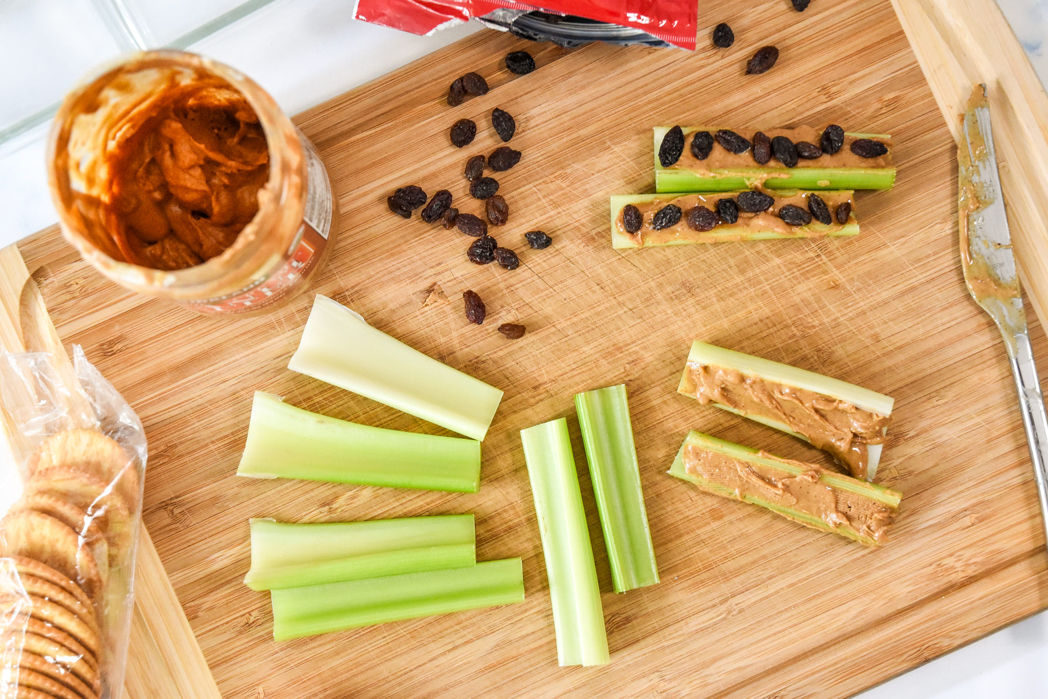 assembling ants on a log with celery, peanut butter and raisins on a cutting board.