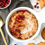a bowl of instant pot gingerbread oatmeal with milk and pomegranate seeds topping.