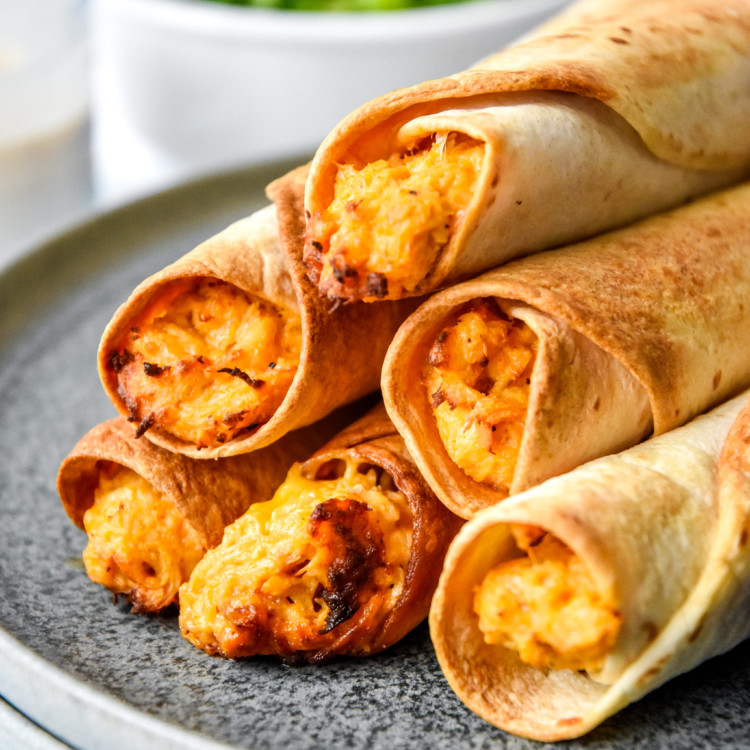 air fryer buffalo chicken flautas cooked and stacked on a plate.