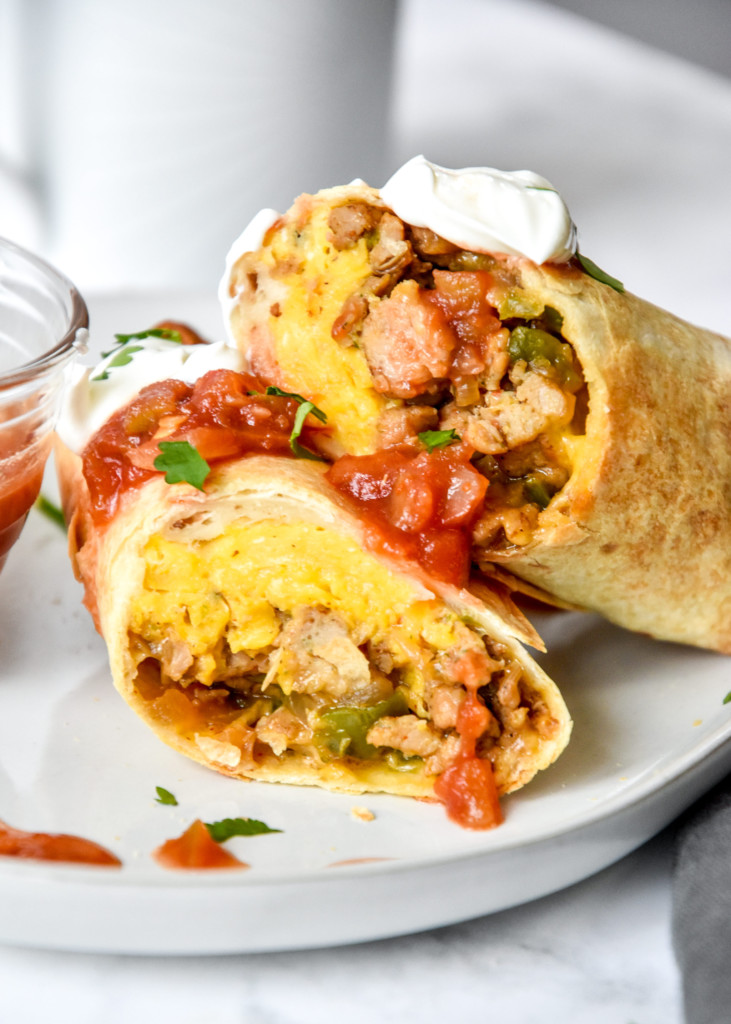 cut in half breakfast burrito topped with salsa and sour cream.