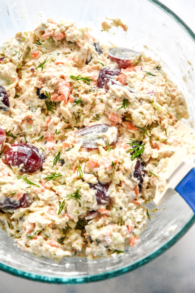 easy chicken salad with grapes mixed up in a glass mixing bowl with a rubber spatula.