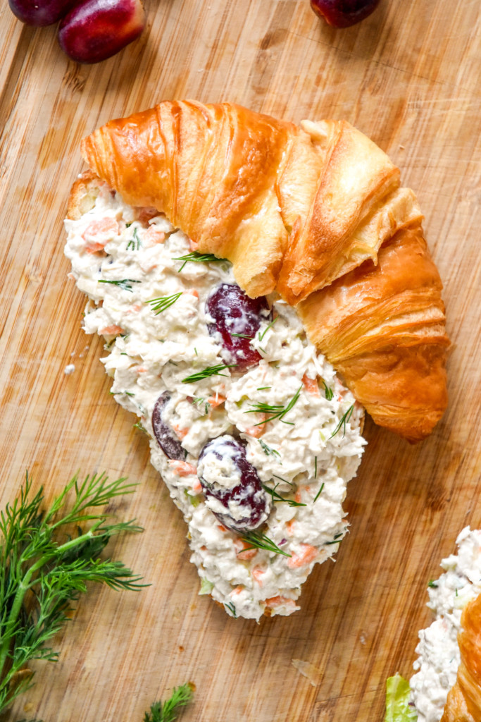 croissant with easy chicken salad with grapes on top on a cutting board.