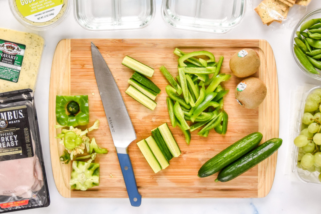 top view of cutting green produce on a cutting board including cucumbers and bell peppers.