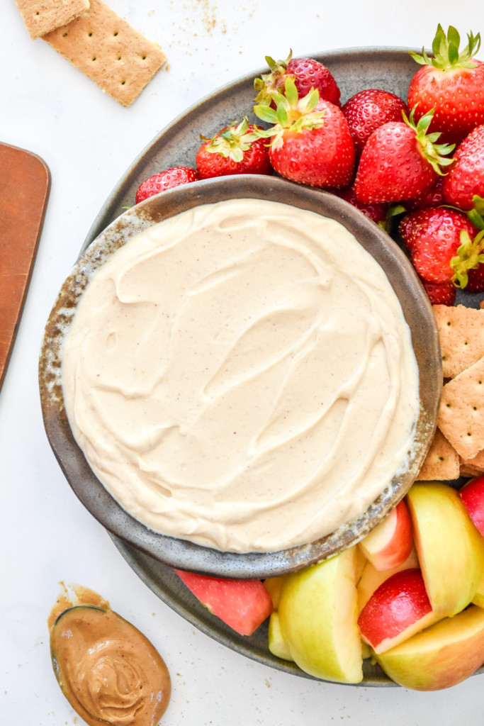 top down photo of peanut butter greek yogurt fruit dip on a plate with fruit and graham crackers.