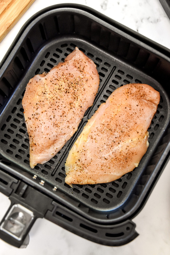 raw chicken breasts in the air fryer basket before cooking.