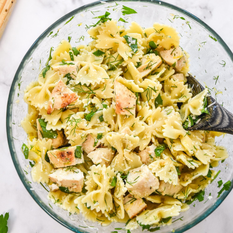 mixed up herby lemon chicken pasta salad in a glass bowl.