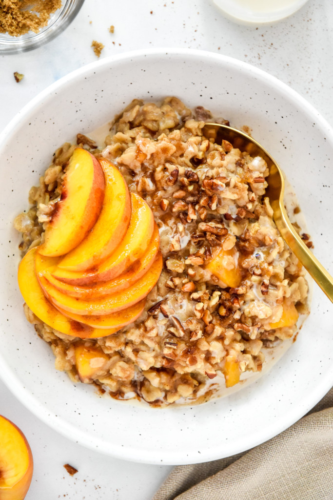 bowl of peaches and cream oatmeal with fresh peaches and a gold spoon.