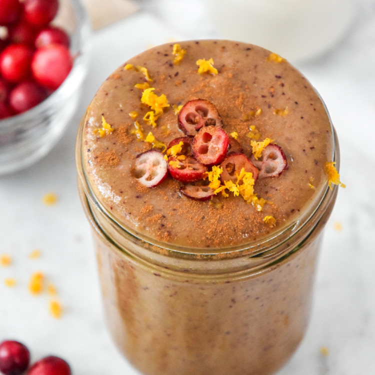 Cranberry Orange Cinnamon Holiday Smoothie topped with sliced cranberries and orange zest in a glass mason jar.