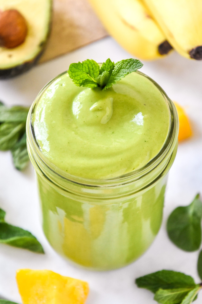 creamy avocado mint green smoothie in a mason jar with a mint leaf on top.