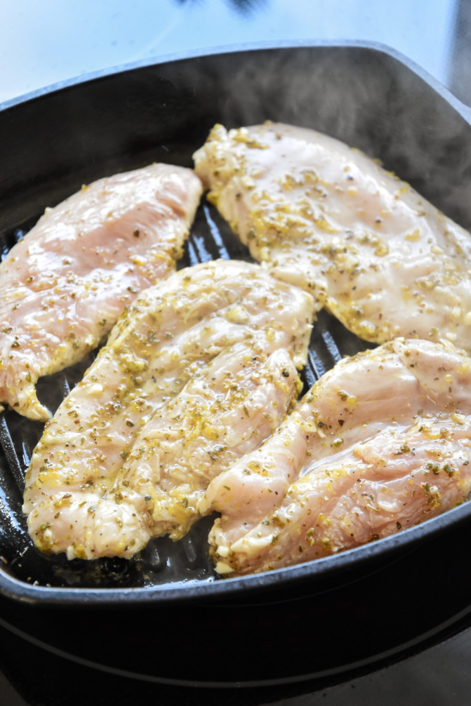 cooking marinated chicken in a cast iron grill pan for the greek chicken salad meal prep bowls.