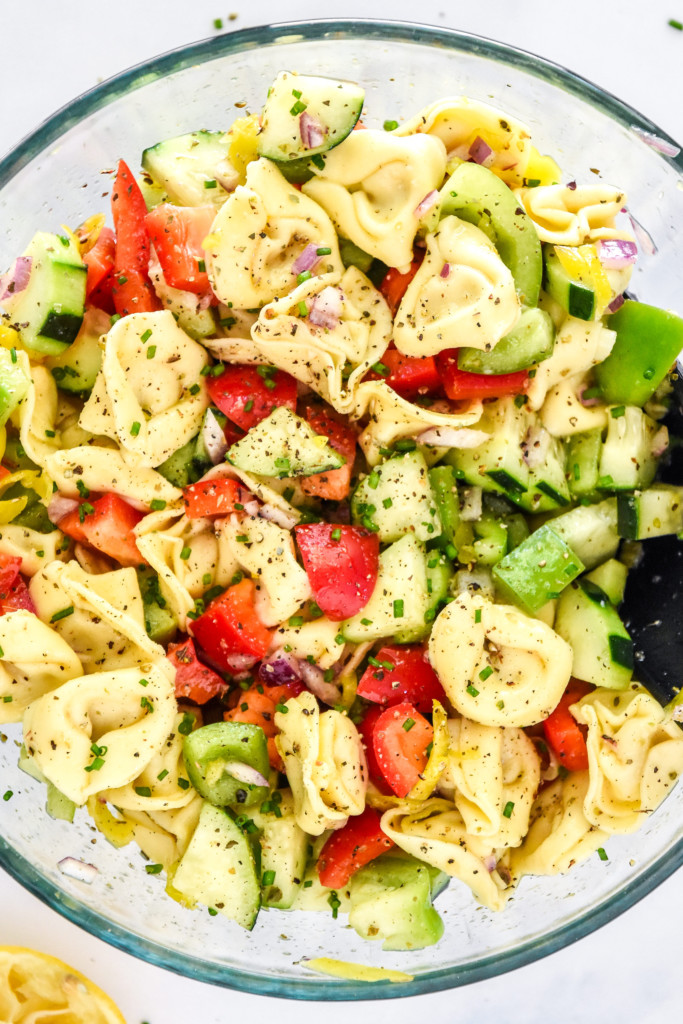 zesty italian tortellini pasta salad in a glass bowl with serving spoon.