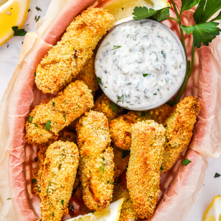 baked cod fish sticks with yogurt tartar sauce in a basket lined with food paper.