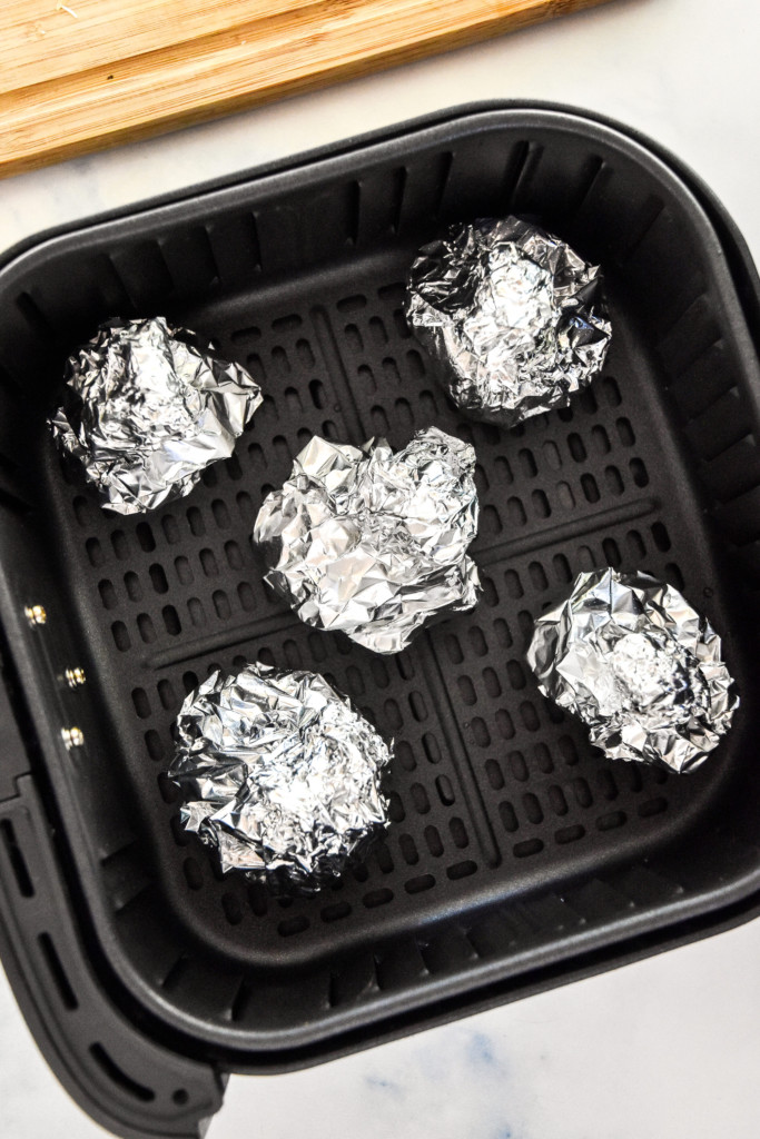 garlic heads in foil in the basket of an air fryer