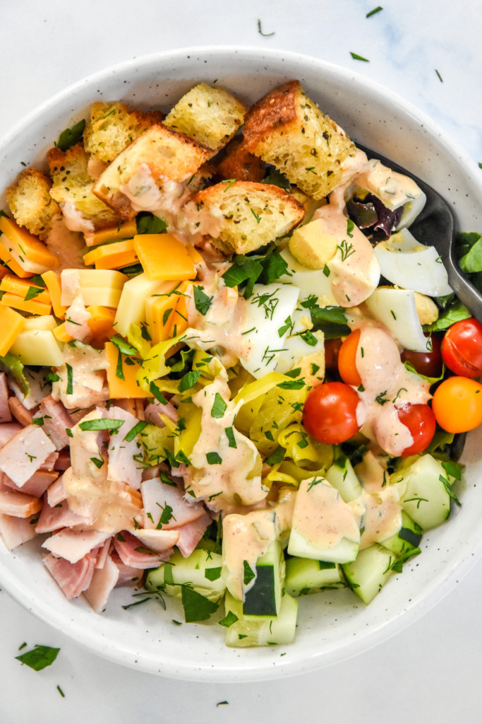 plated chef salad with fresh veggies, croutons, meat and cheese on a bed of romaine with dressing.