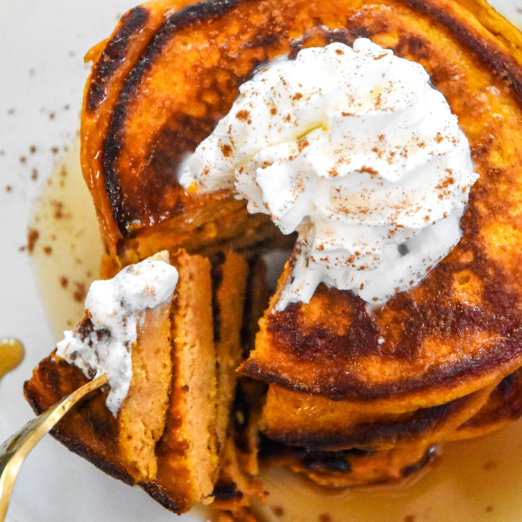 Pumpkin pie greek yogurt pancakes on a plate with whipped cream on top.