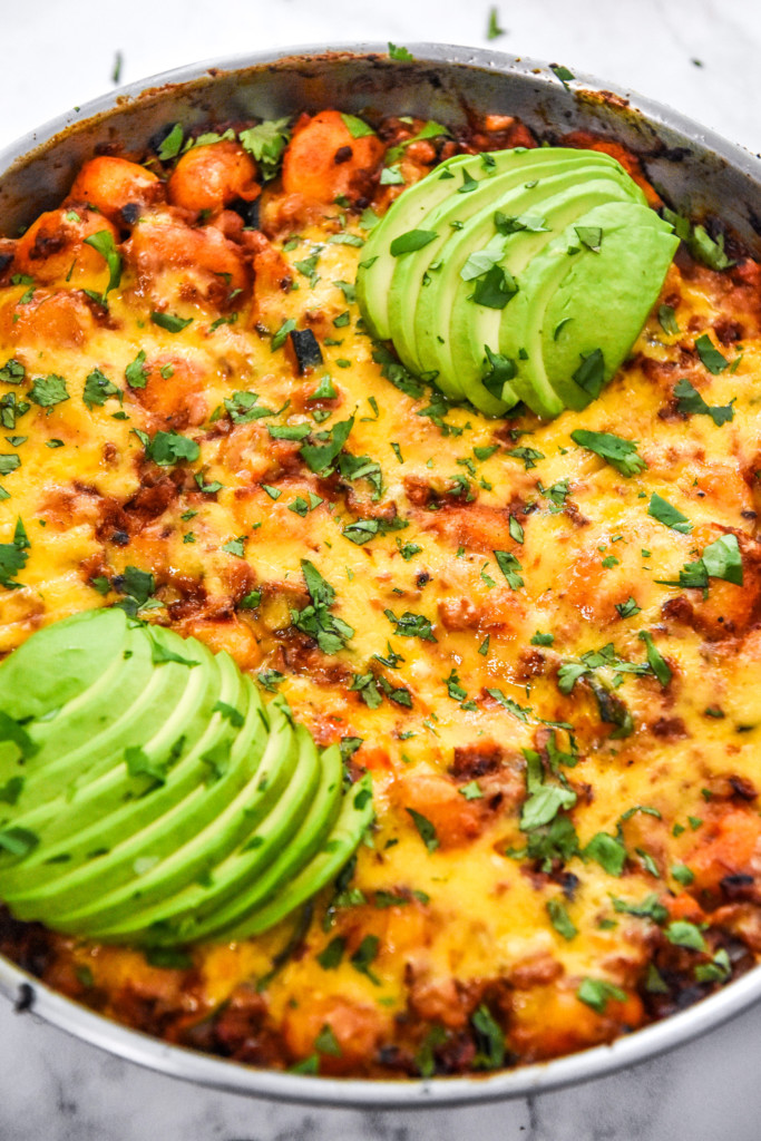close up of the cooked one-pan soy chorizo gnocchi skillet with melted cheese and avocado on top.