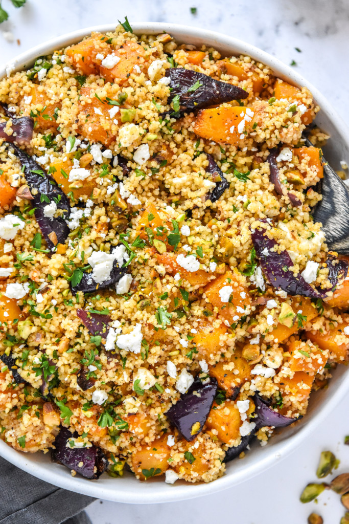 roasted butternut squash couscous salad in a glass bowl with a wooden spoon.