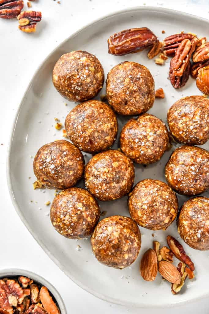 no-bake pecan pie date balls on a plate with pecans and dates as decoration.