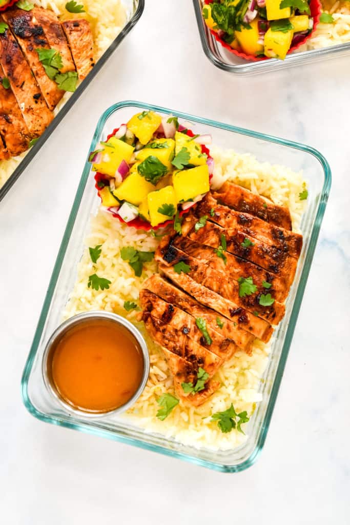 chipotle lime chicken meal prep in a glass rectangle container with mango salsa and dressing.