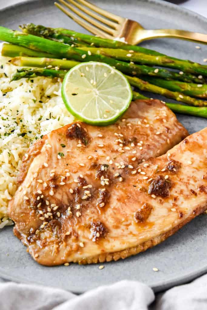 baked tilapia on a plate with rice and asparagus.
