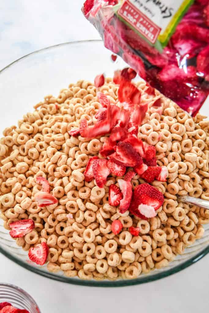 pouring cheerios and freeze-dried strawberries into a large mixing bowl.