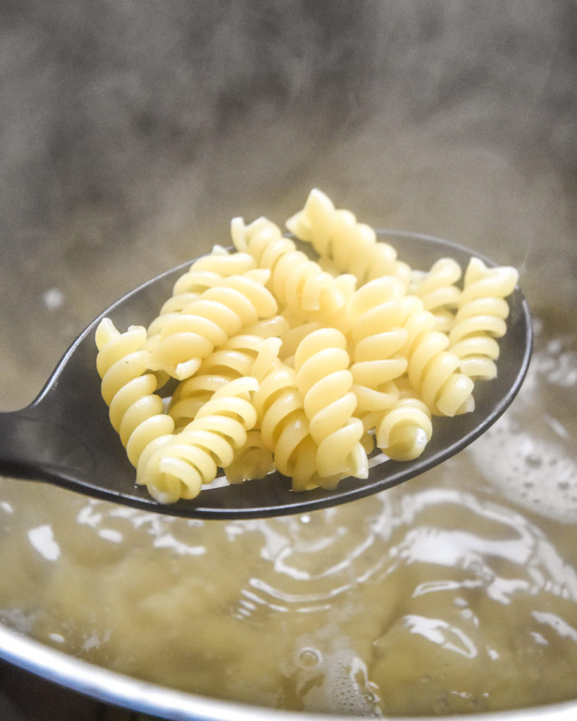 boiled rotini pasta in a slotted spoon over boiling water.
