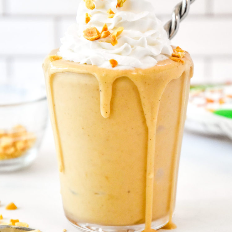 A Peanut Butter Powder Milkshake in a clear cup with whipped cream and chopped peanuts on top.