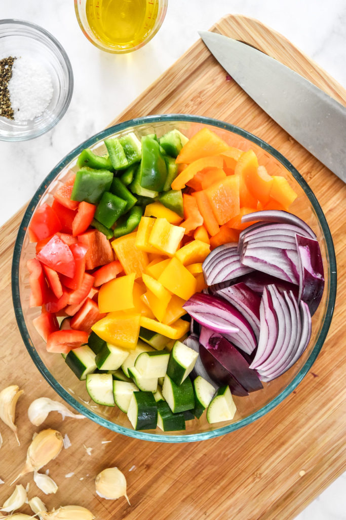 large glass bowl of cut veggies on a wood cutting board.