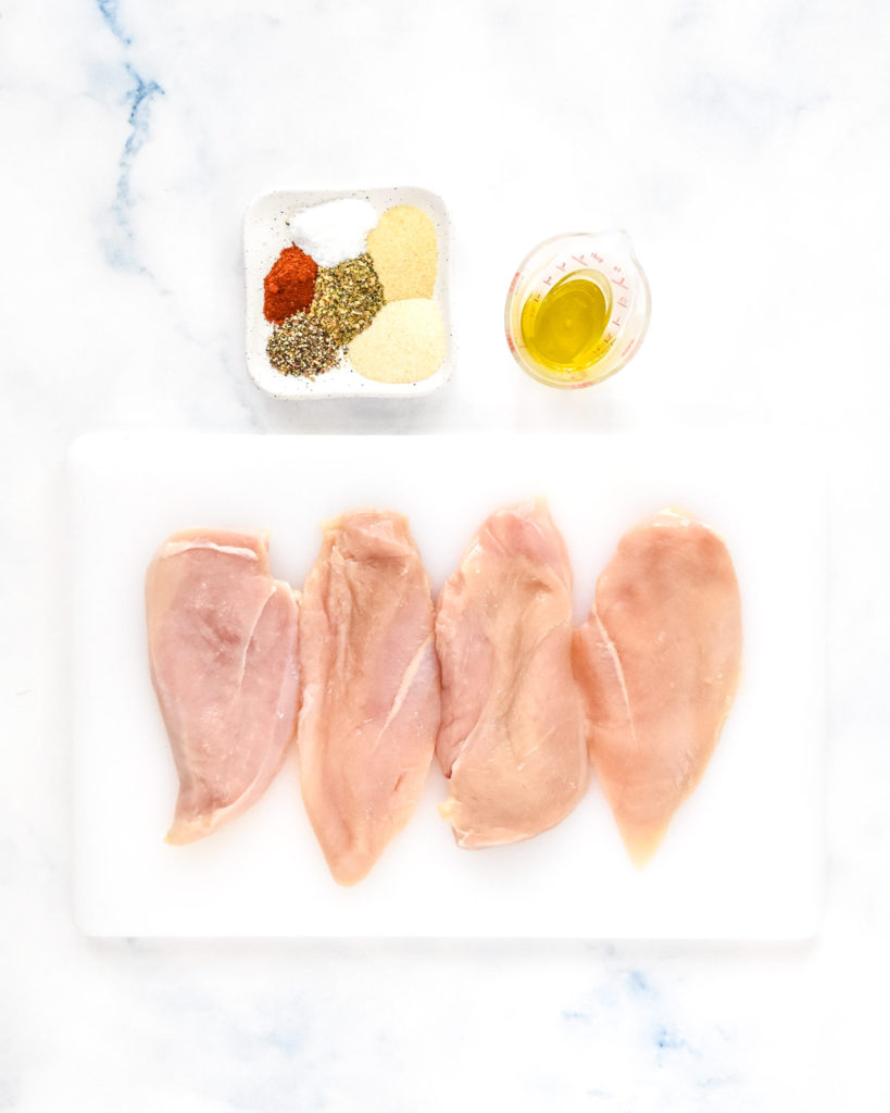 raw chicken breasts on a cutting board with seasonings and oil on the side.