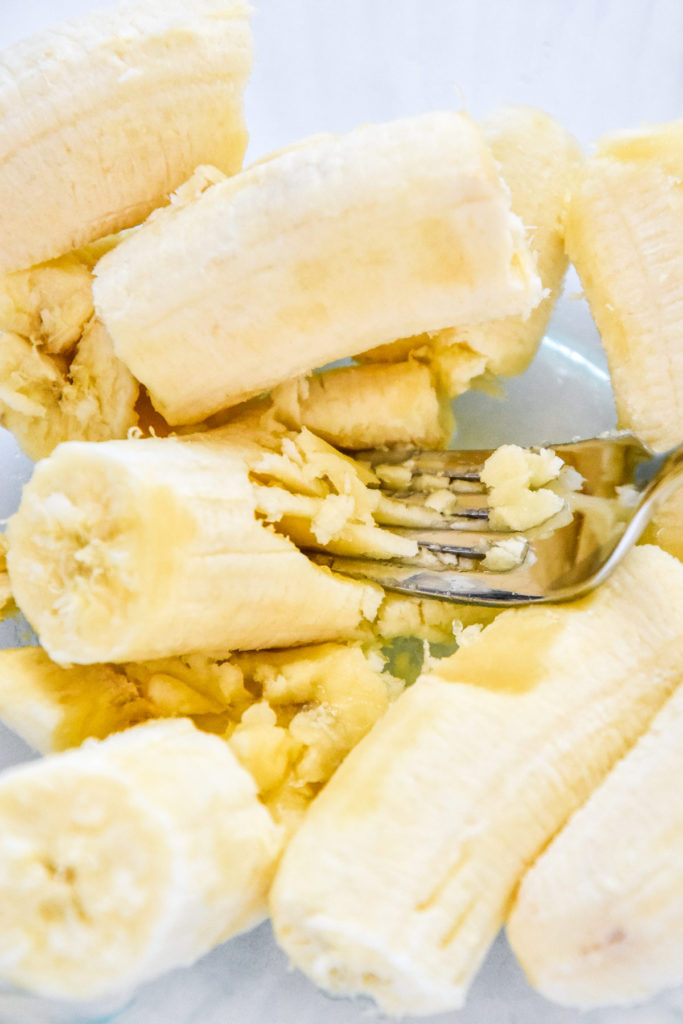 mashing bananas with a fork in a glass bowl.