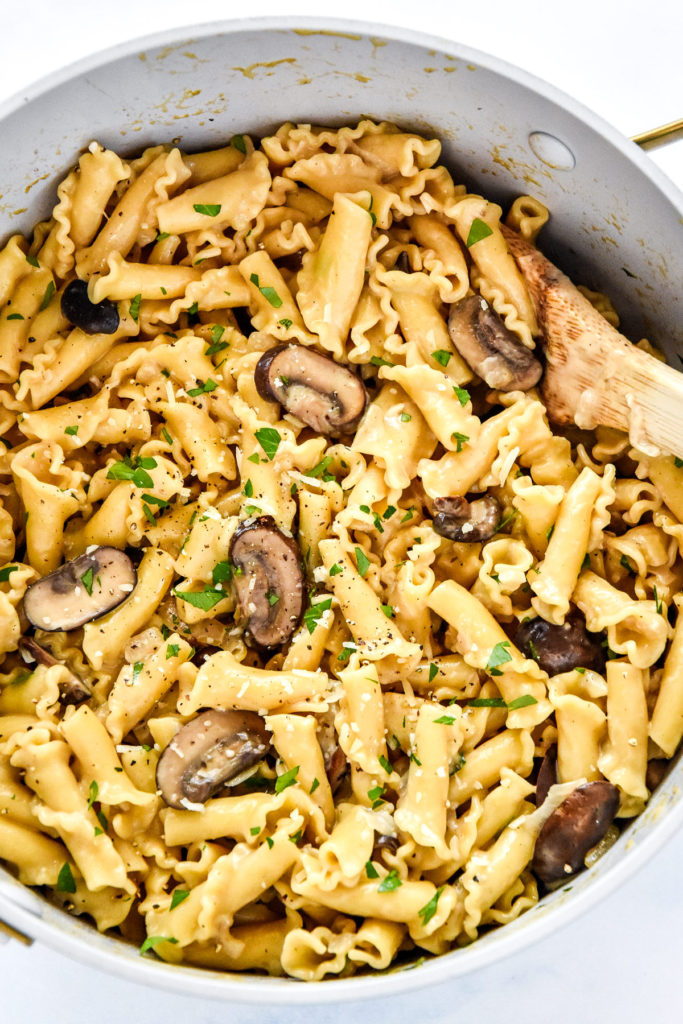 one pot creamy mushroom pasta with parmesan and parsley on top and wooden spoon in the pot.