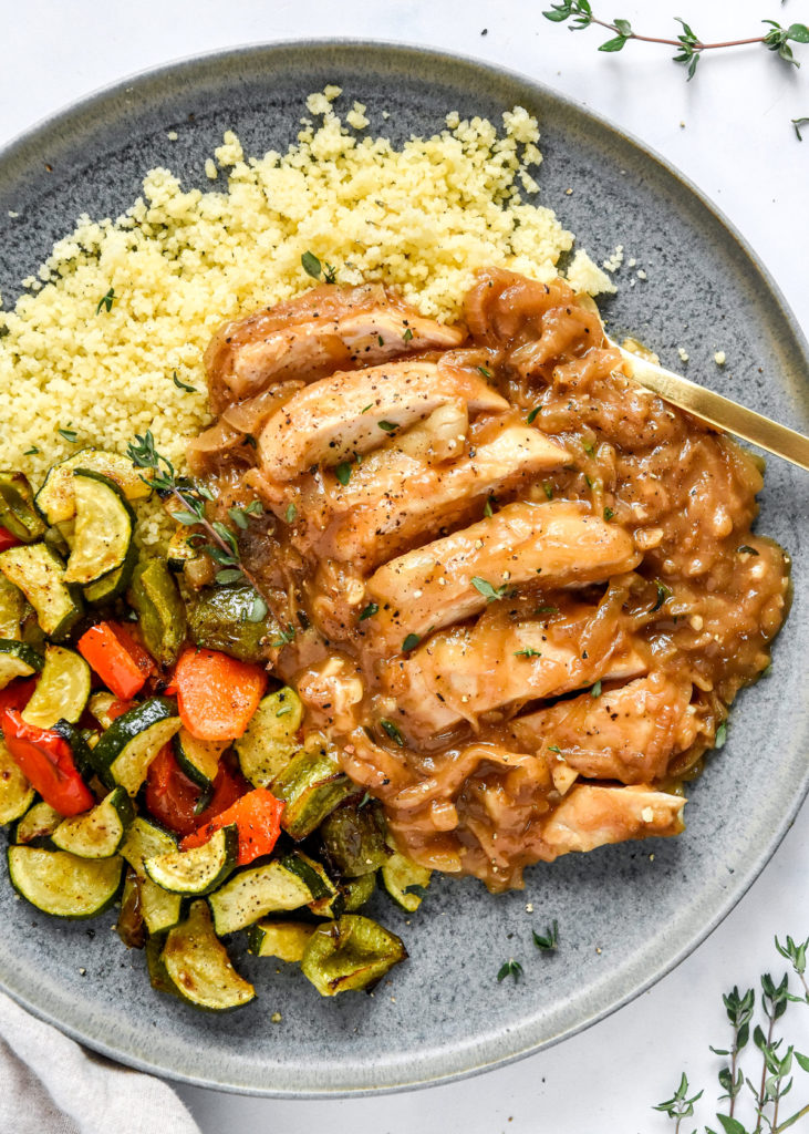 french onion baked chicken breast sliced on a plate with veggies and couscous.