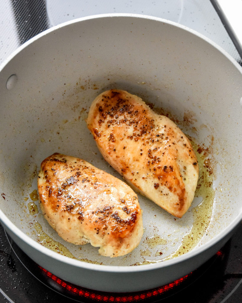 browning seasoned chicken breasts in a soup pot on the stove.