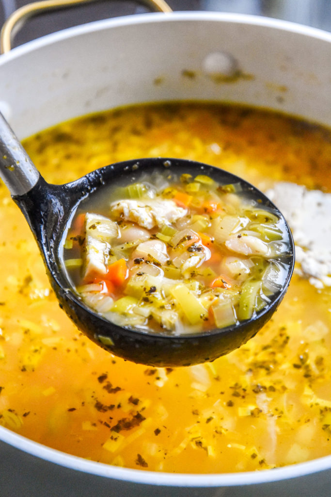 a ladle full of white bean lemon chicken soup over the soup pot.