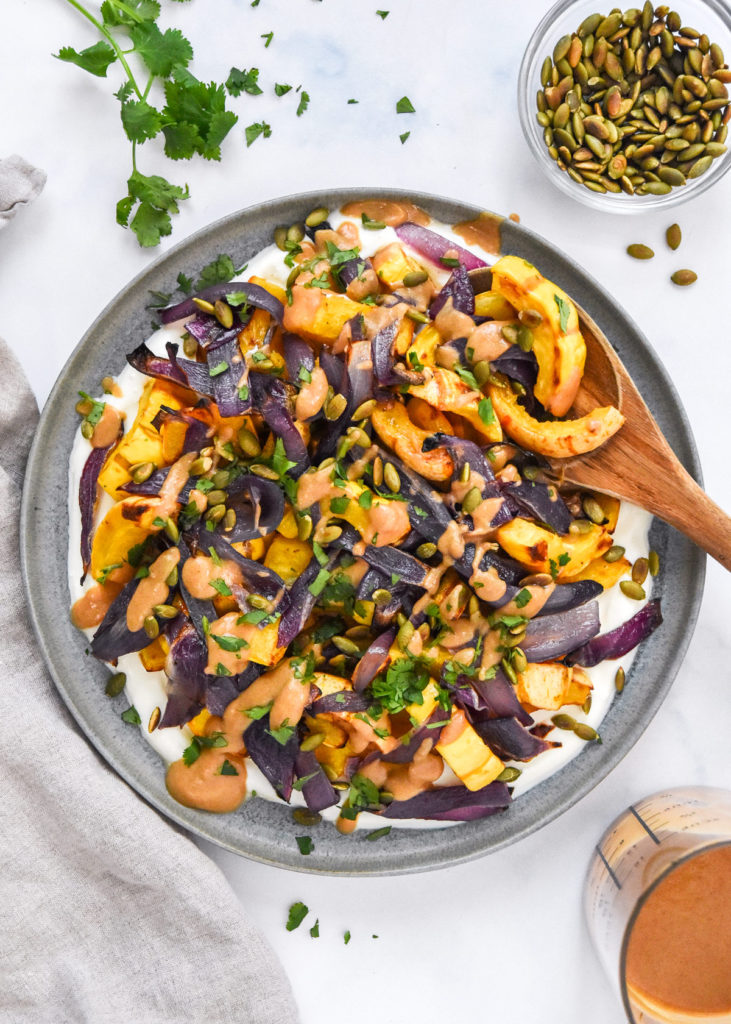 roasted squash salad with whipped feta on a plate with a wooden spoon.