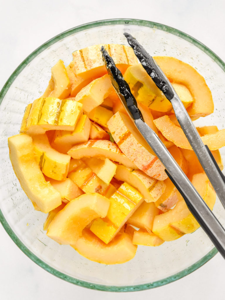 cut delicata squash in a bowl with oil and seasoning.