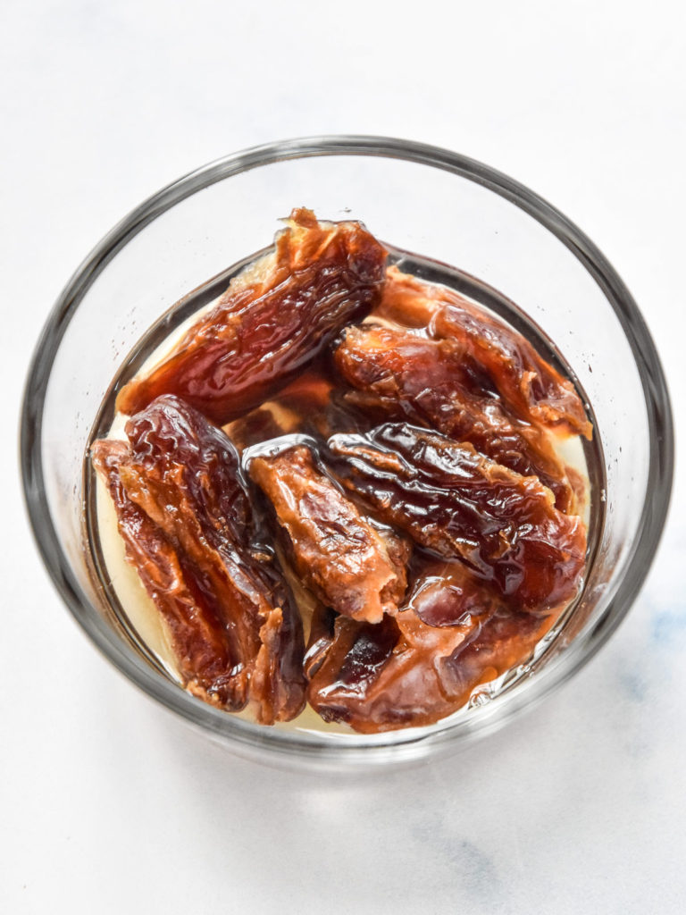 pitted dates soaking in a glass bowl with hot water.