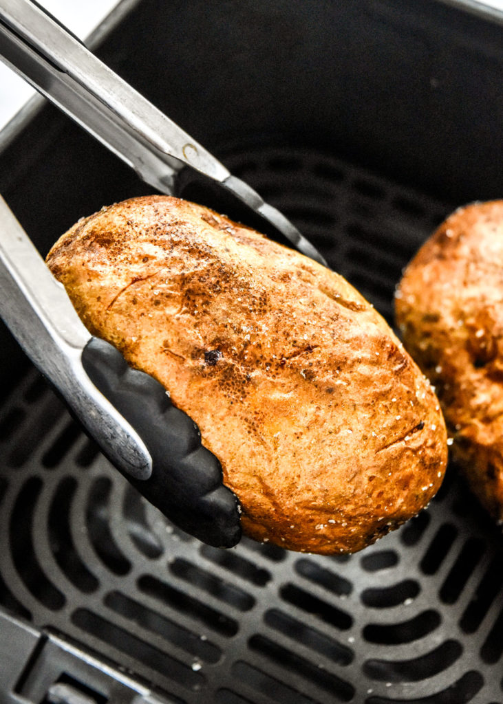 baked potatoes in tongs after being cooked in the air fryer.