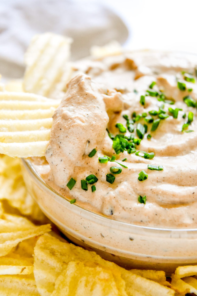 dipping a potato chip into the homemade roasted onion dip.