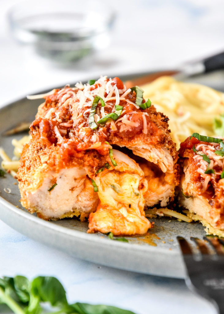 air fryer stuffed chicken parmesan on a plate cut in half with cheese oozing out.